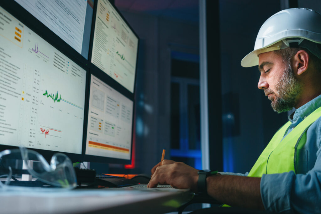 Worker engineer control process of production uses computer with modern SCADA system which showing AI and machine learning. Bearded operator follow of industry process on factory